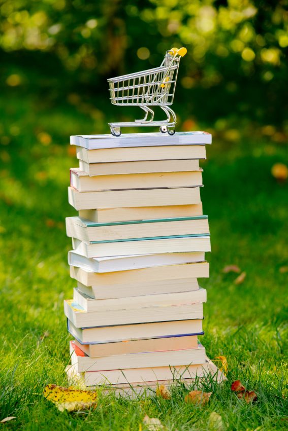 stack of books and shopping cart on the green grass in autumn
